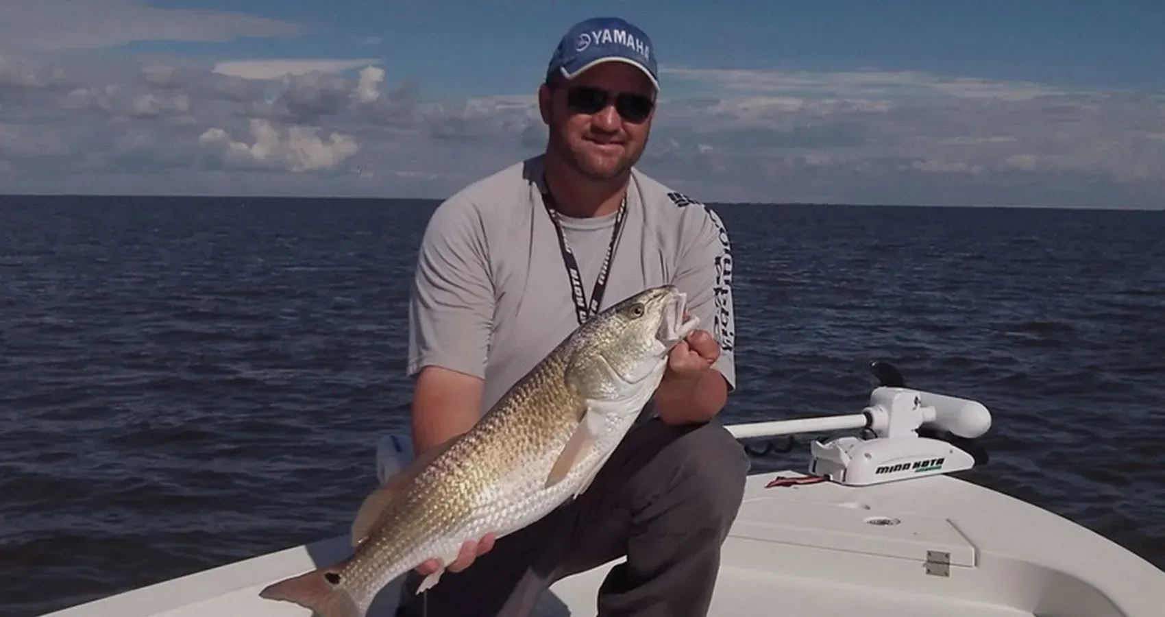 A man is kneeling on a boat holding a large fish.