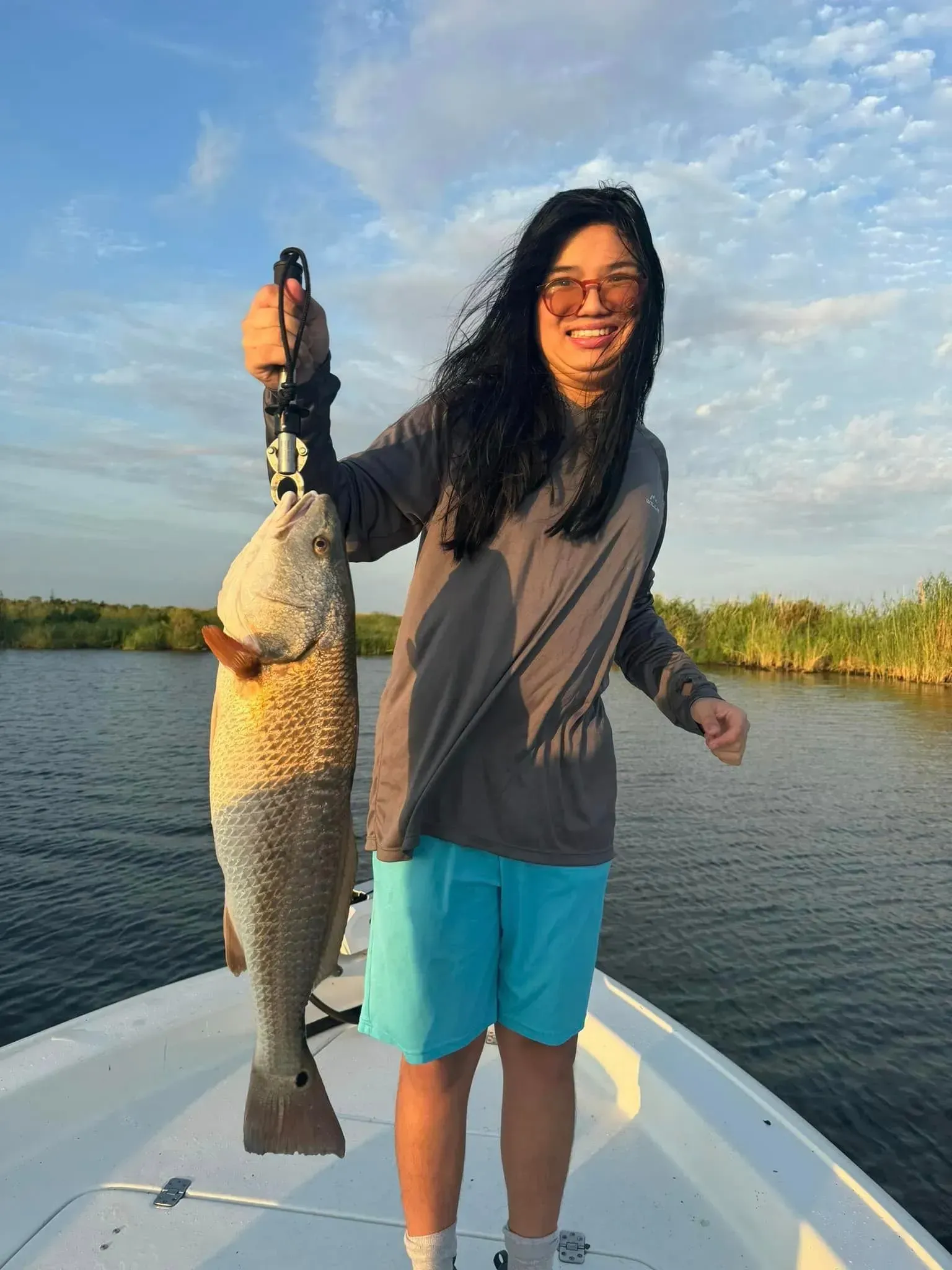 A woman is standing on a boat holding a large fish.