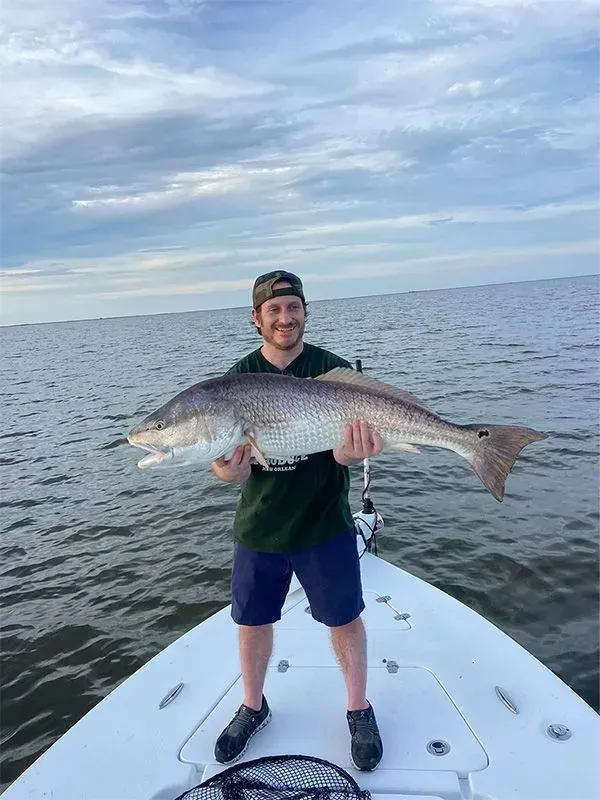 A man is standing on a boat holding a large fish.