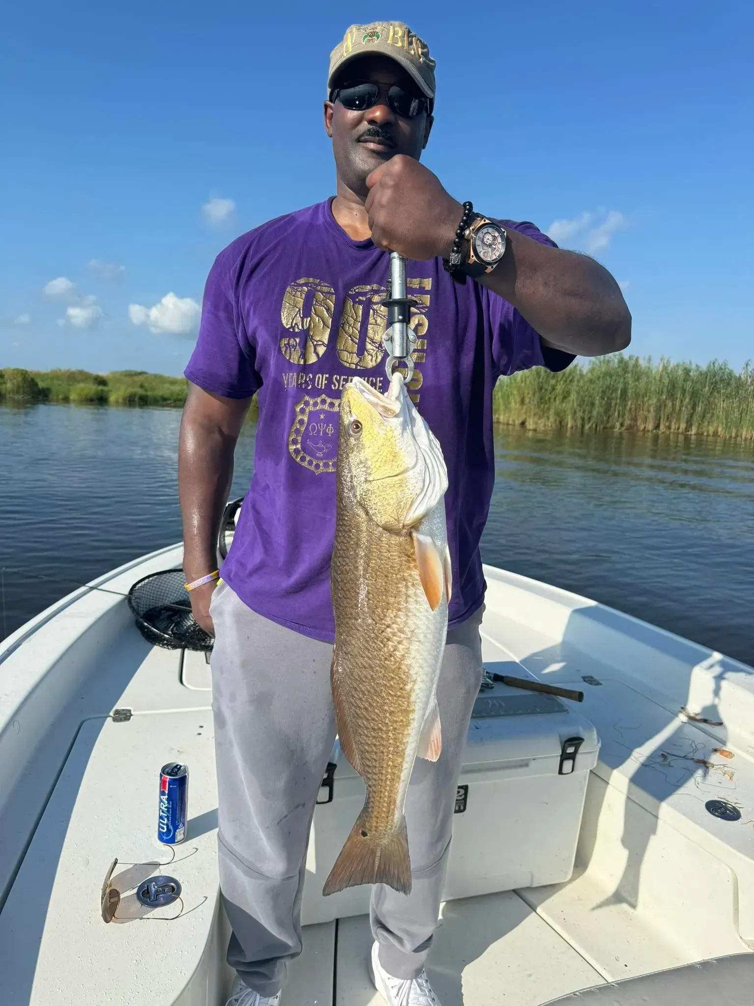 A man in a purple shirt is holding a large fish on a boat.