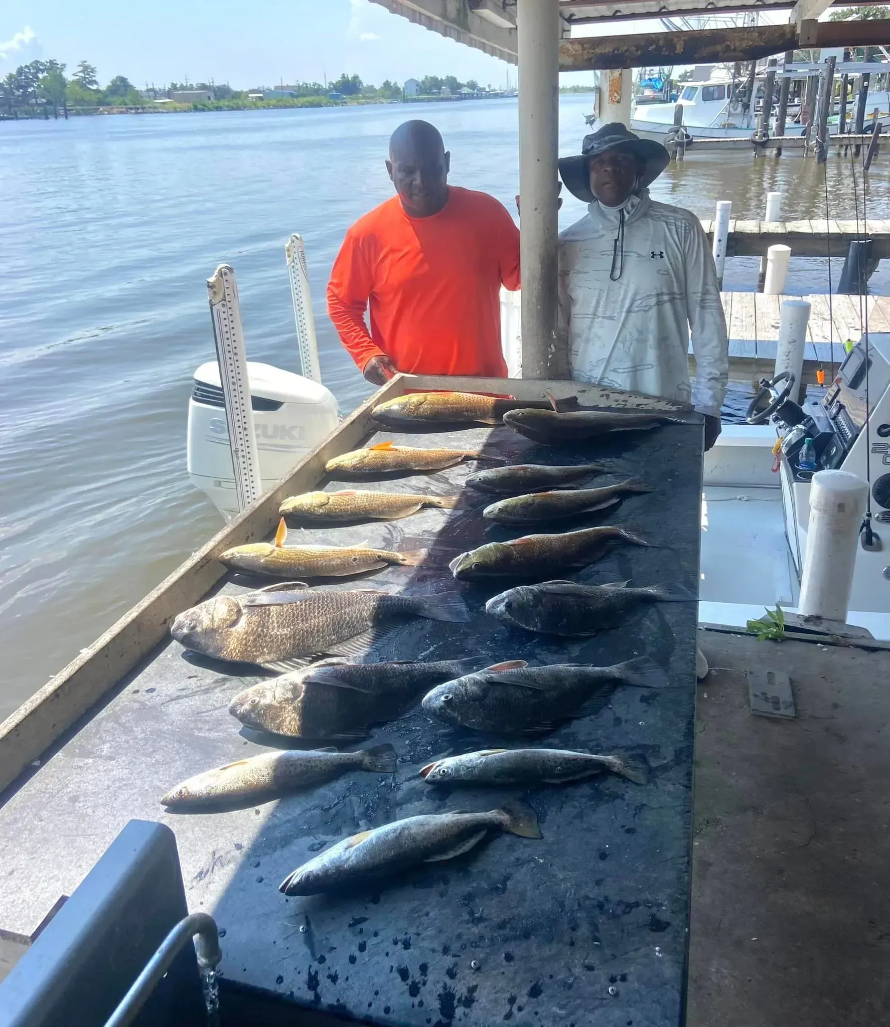 Two men are standing next to a table filled with fish.