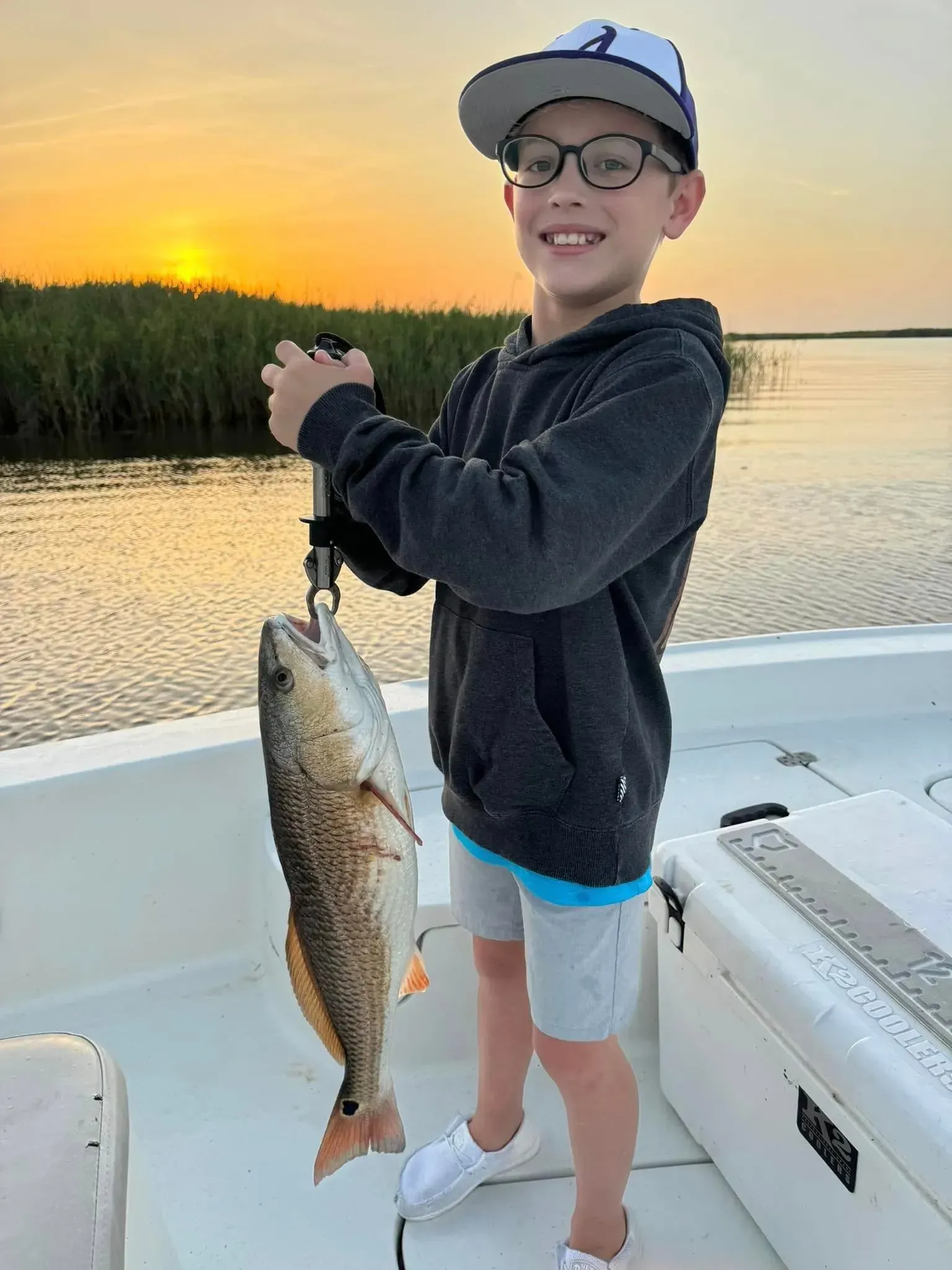 A man and a boy are standing on a boat holding a large fish.