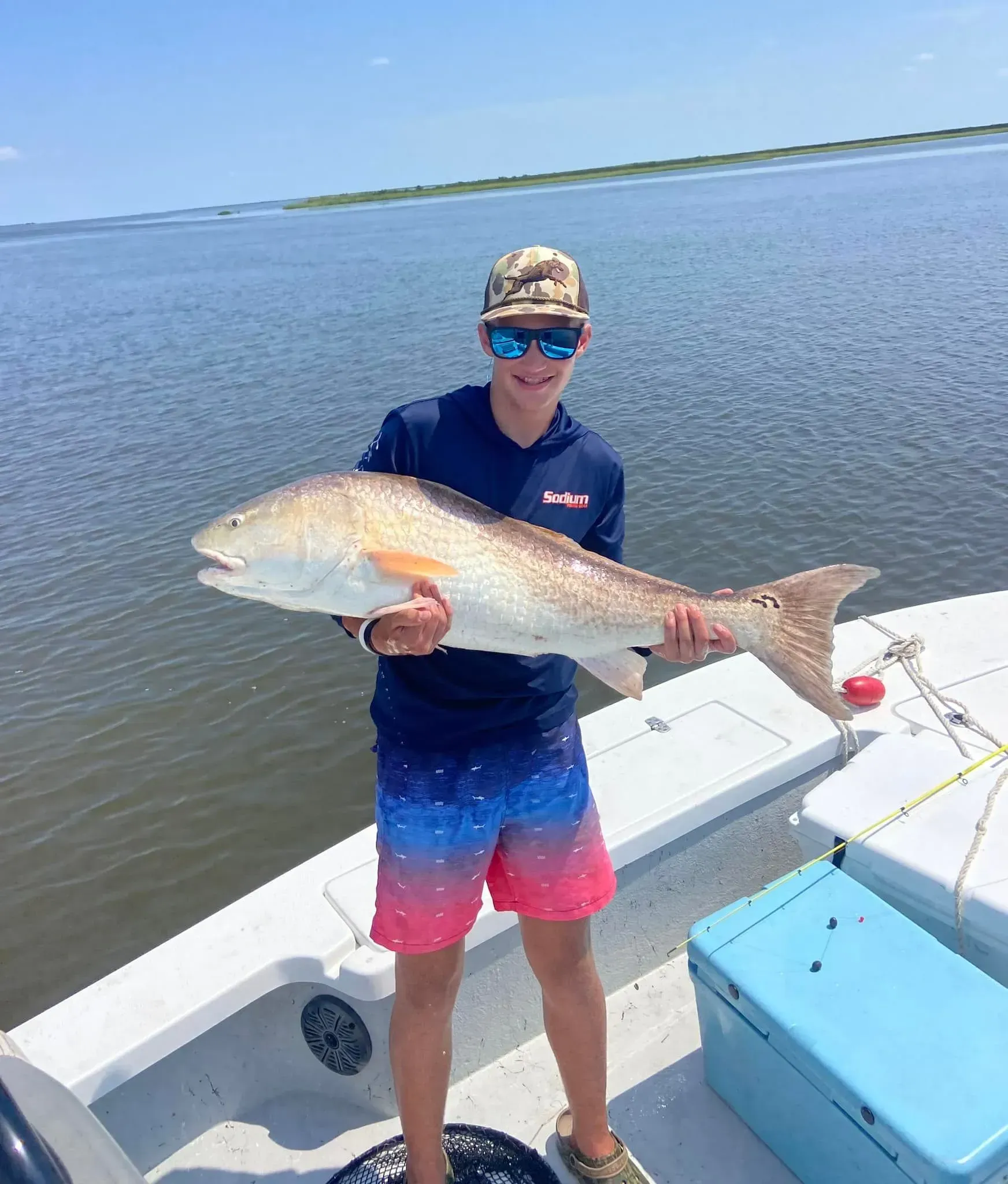 A young man is standing on a boat holding a large fish.