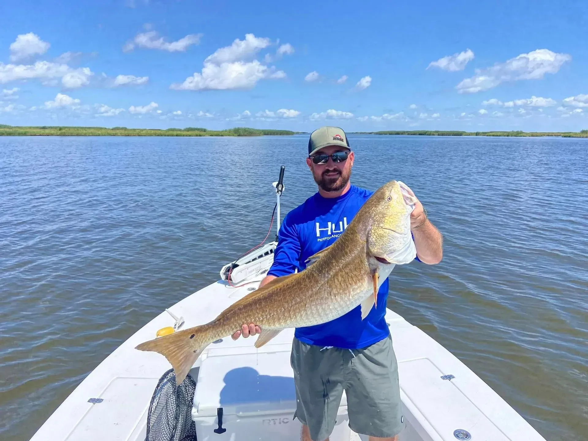 A man is standing on a boat holding a large redfish.