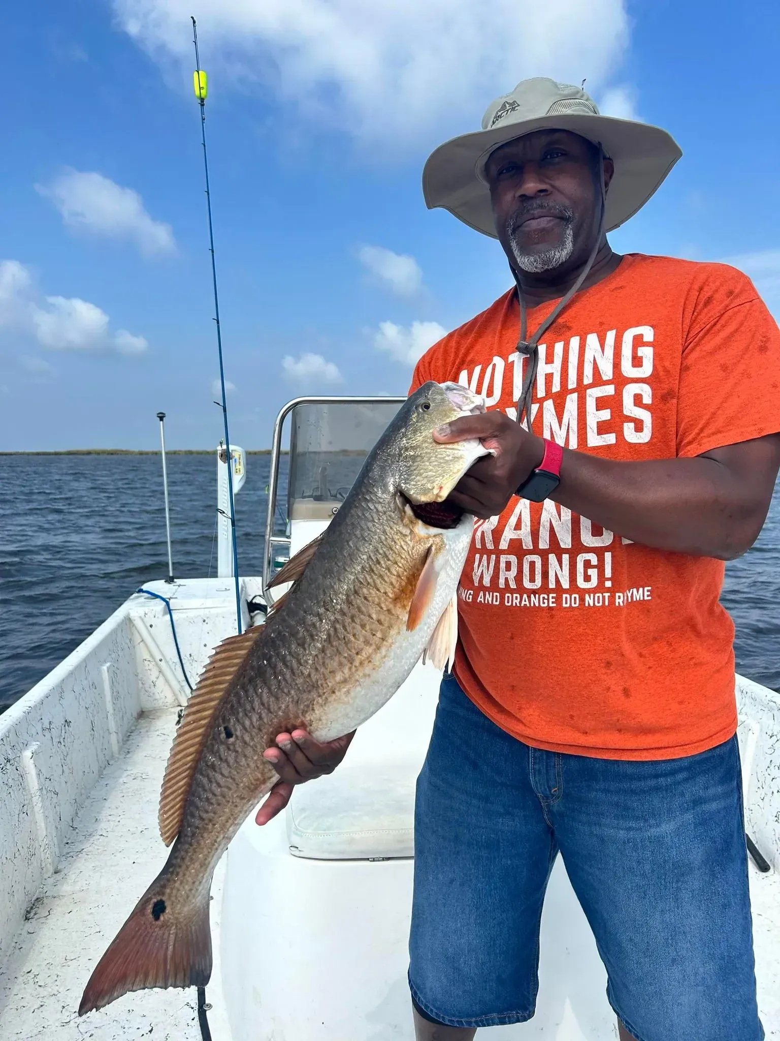 A man in an orange shirt is holding a large fish on a boat.
