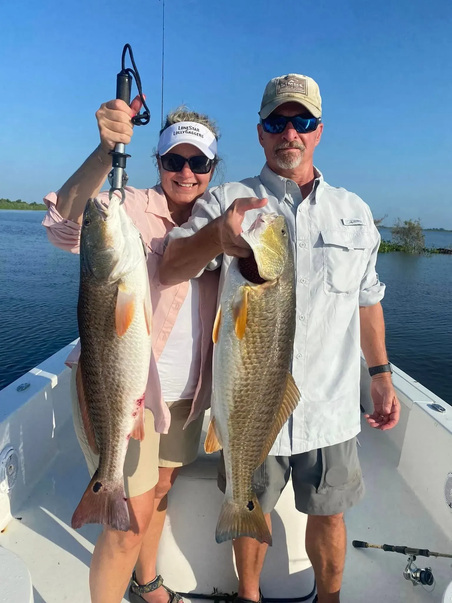 A man and a woman are holding two fish on a boat.