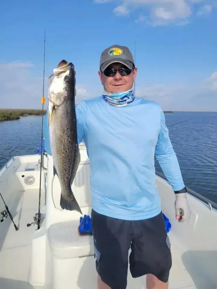 A man is standing on a boat holding a large fish.