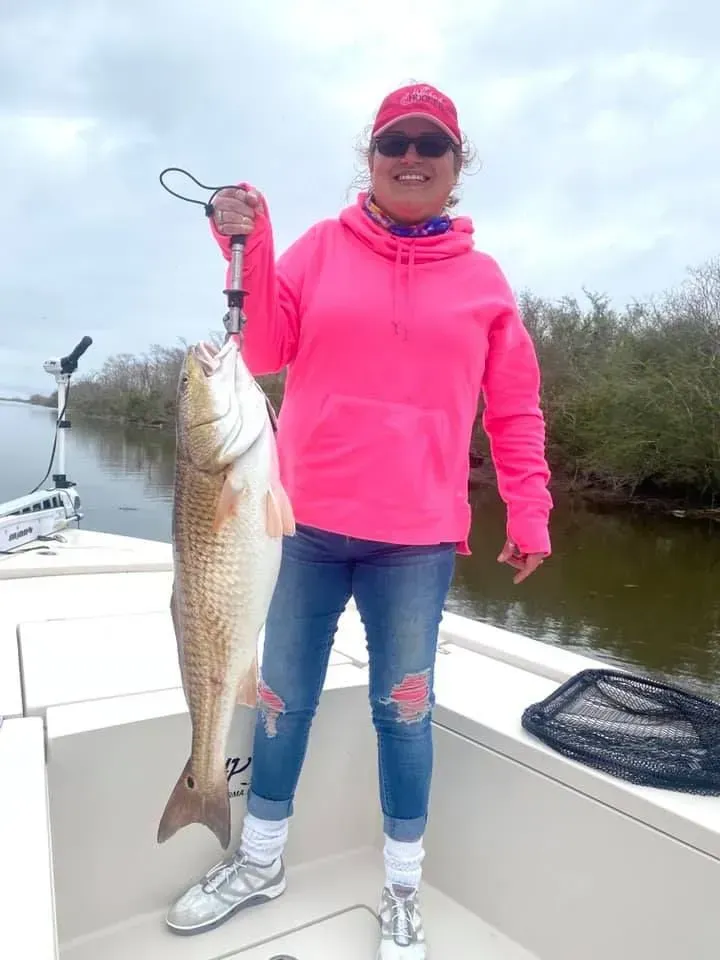 A woman in a pink hoodie is holding a large fish on a boat.
