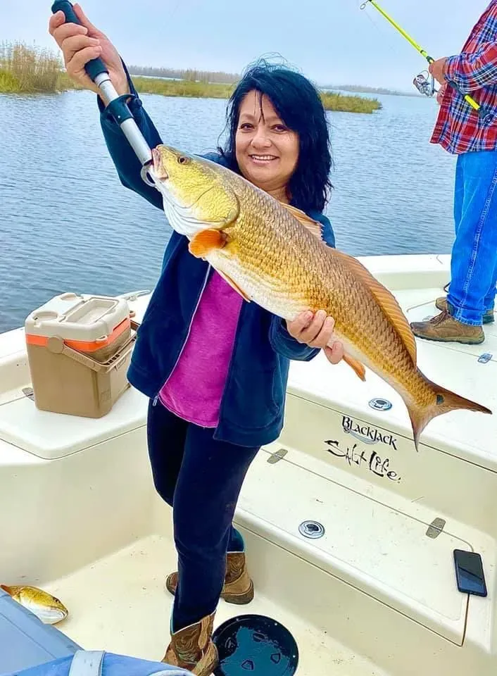 A woman is holding a large redfish on a boat.