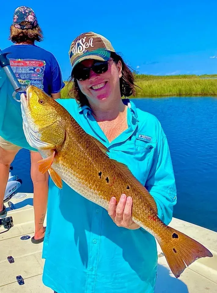 A woman is holding a large red fish on a boat.