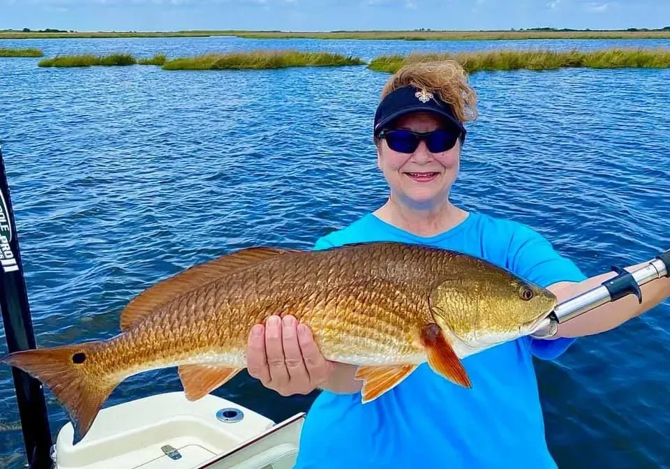 A woman is holding a large redfish on a boat.