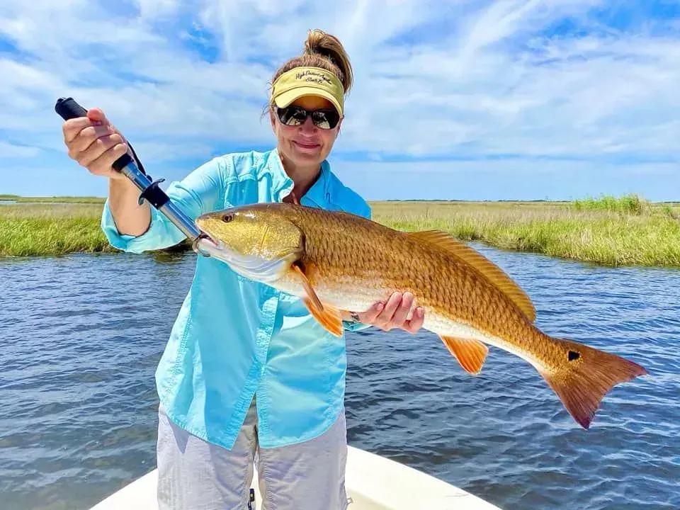A woman is holding a large redfish on a boat.