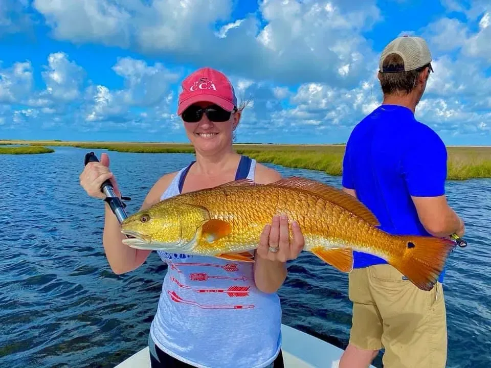 A woman is holding a large redfish on a boat.