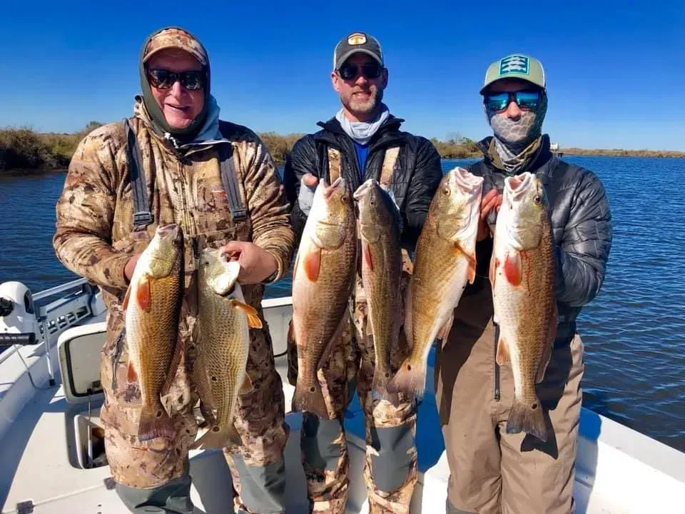 Three men are standing on a boat holding fish.