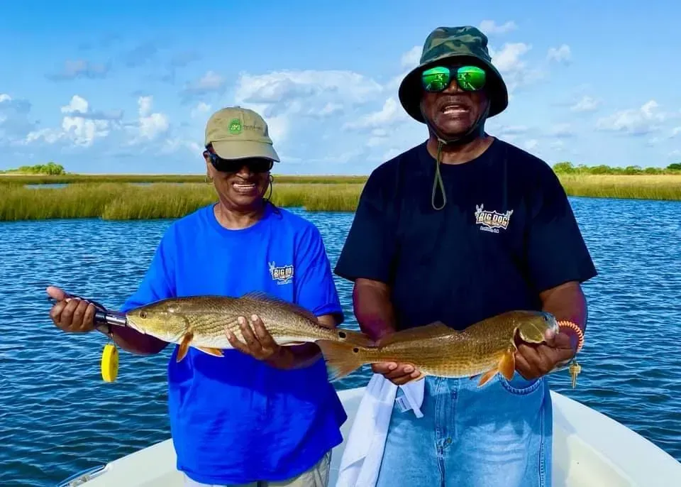 Two men are standing on a boat holding two fish.