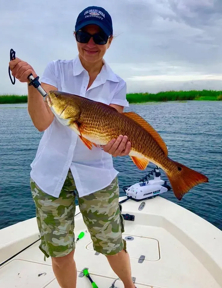 A woman is standing on a boat holding a large fish.