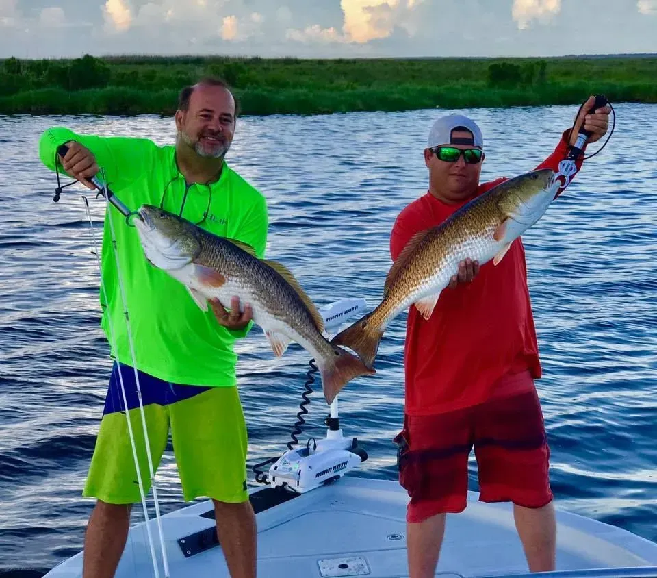 Two men are standing on a boat holding fish in their hands.