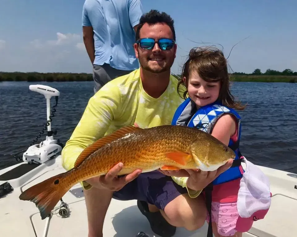 A man and a little girl are holding a large fish on a boat.