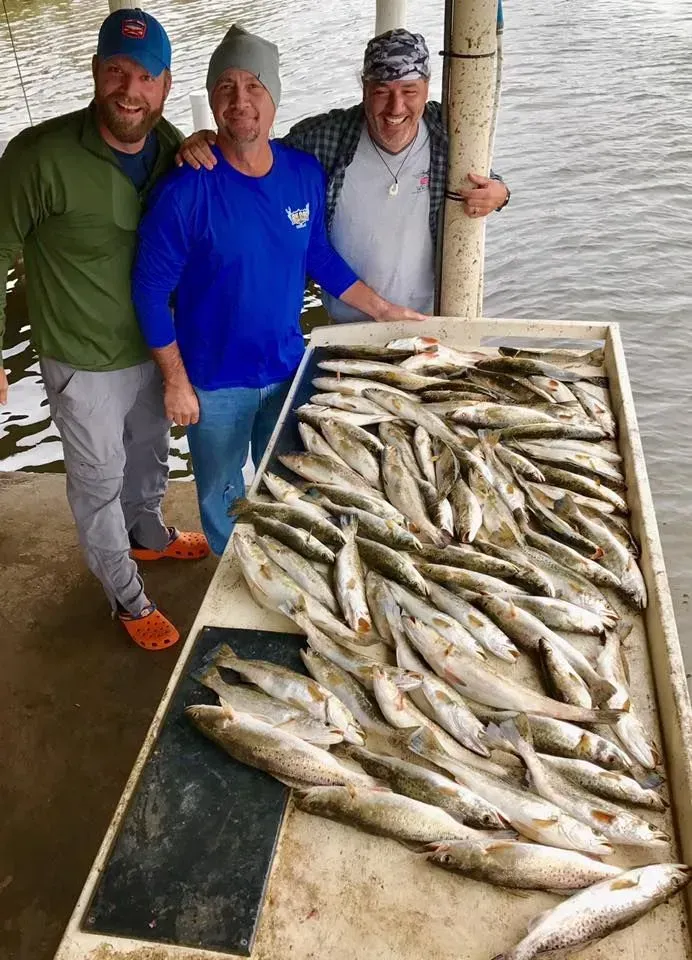 Three men are standing next to a table filled with fish.