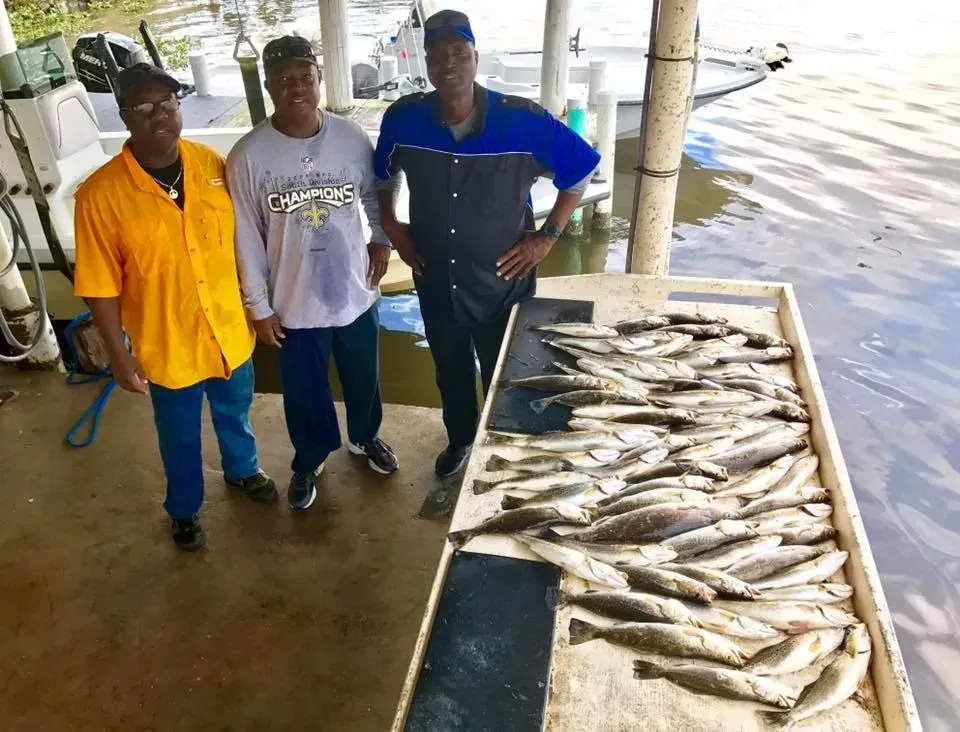 Three men are standing next to a table full of fish.