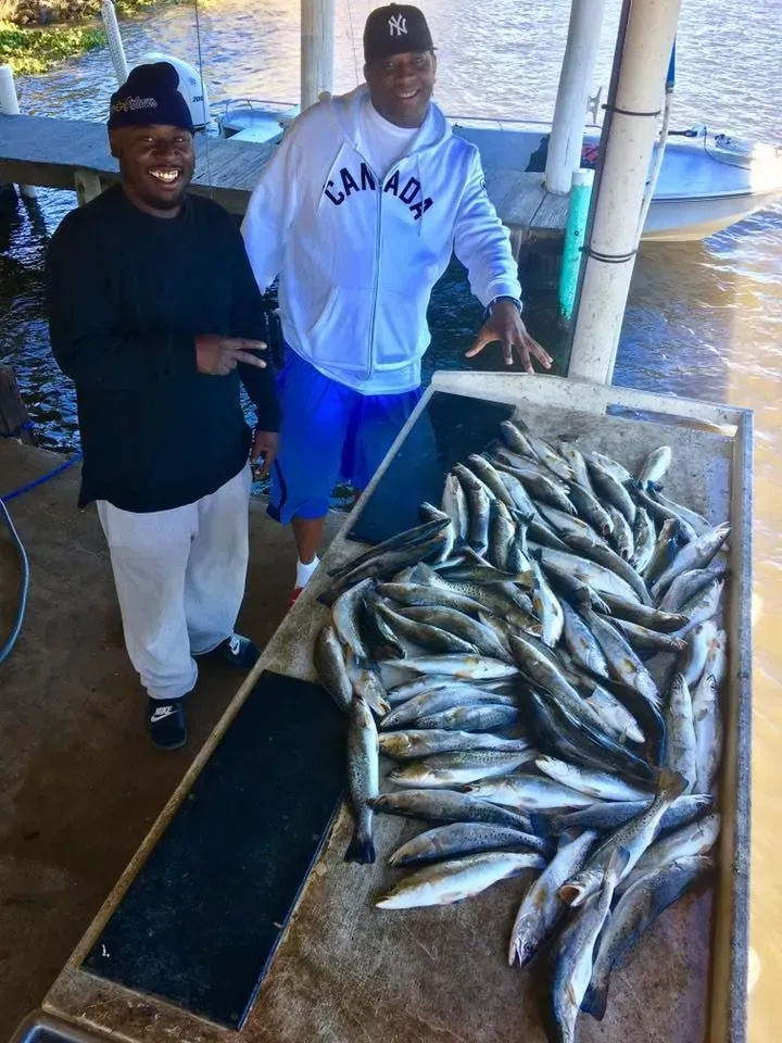 Two men are standing next to a table full of fish.