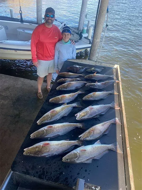 A man and a boy are standing next to a table full of fish.