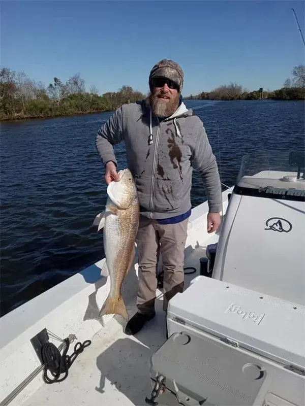 A man is standing on a boat holding a large fish.