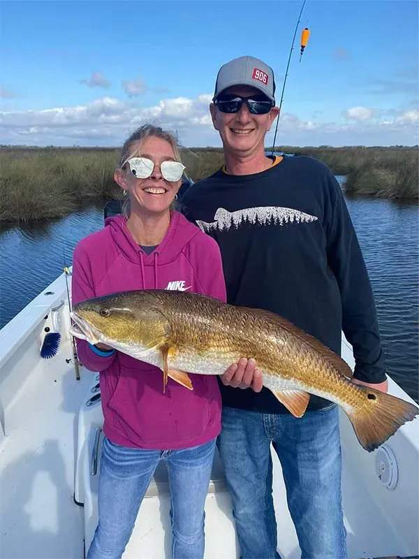 A man and a woman are standing on a boat holding a large fish.