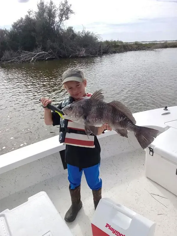 A young boy is holding a large fish on a boat