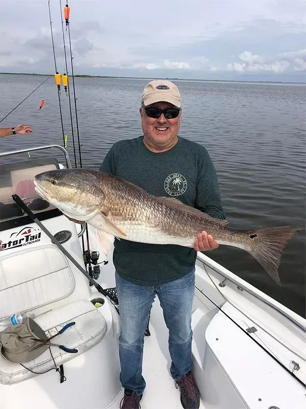 A man is standing on a boat holding a large fish.