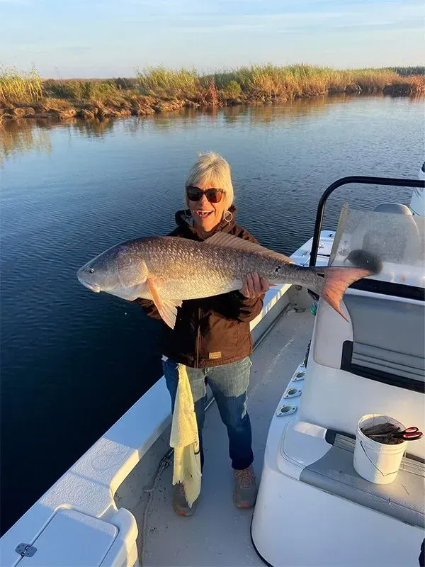 A woman is standing on a boat holding a large fish.