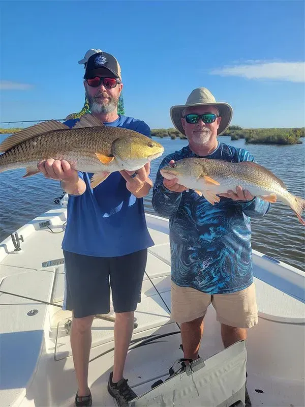 Two men are standing on a boat holding two fish.