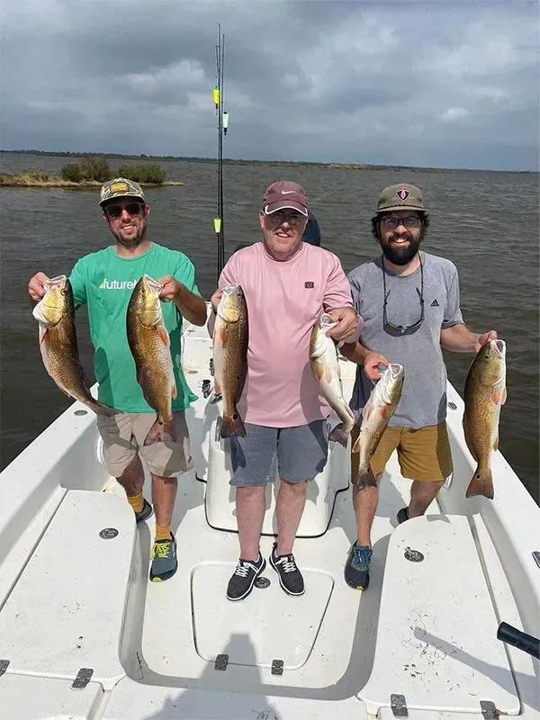 Three men are standing on a boat holding fish.
