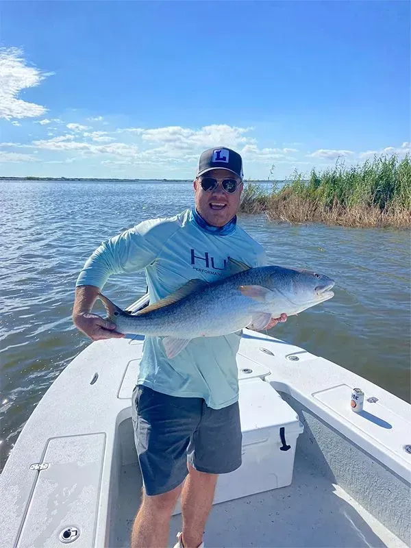 A man is standing on a boat holding a large fish.
