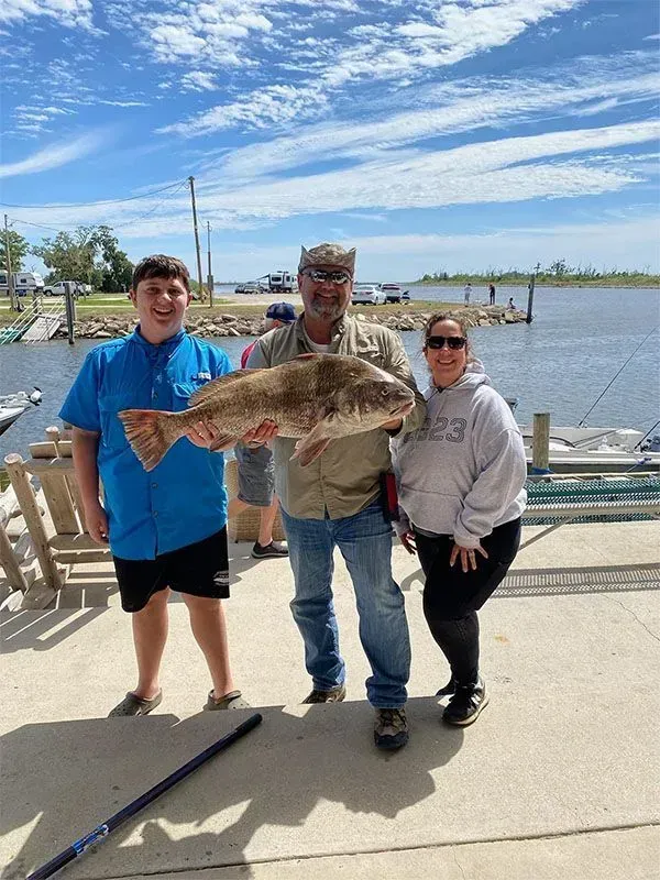 A man and two children are holding a large fish on a dock.