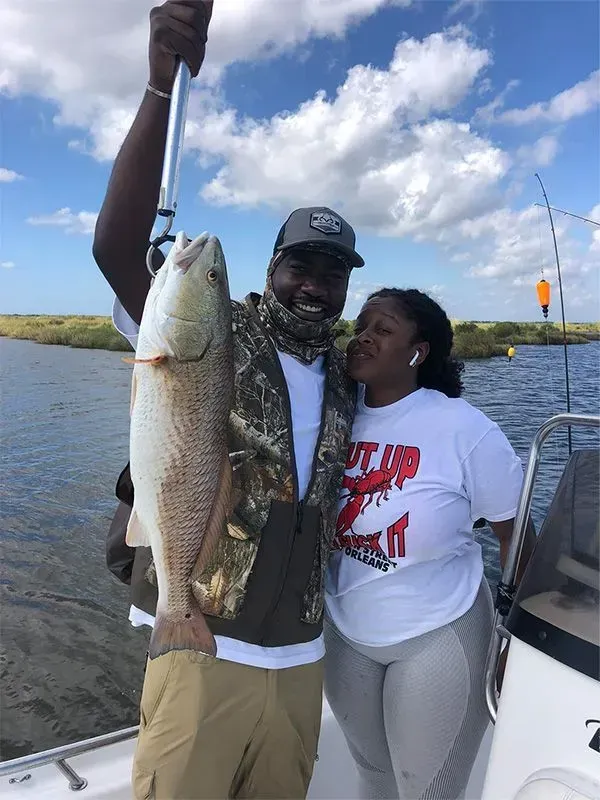 A man and a woman are standing on a boat holding a large fish.