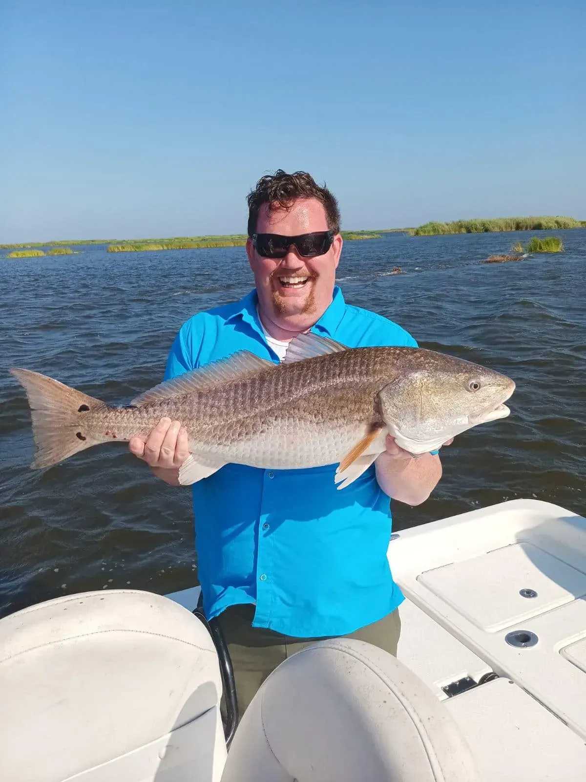 A man is holding a large redfish on a boat.