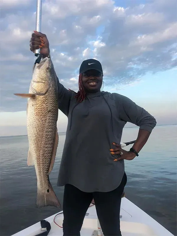 A woman is standing on a boat holding a large fish.
