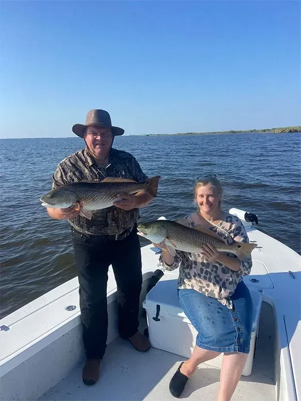 A man and a woman are holding large fish on a boat.