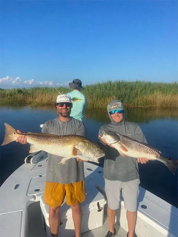 Two men are standing on a boat holding two large fish.