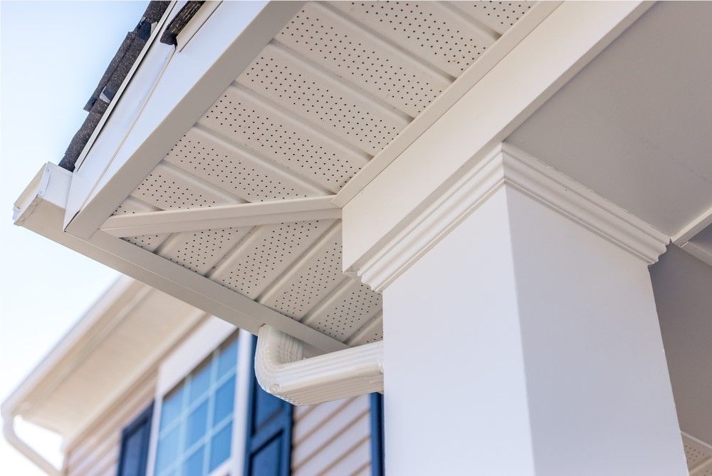 Close-up view of a white porch column and soffit with ventilation holes. A rain gutter and window frame are visible.