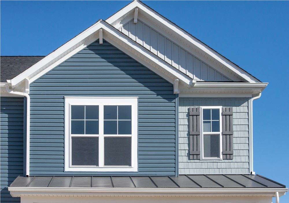 Blue house exterior with a large window, small window with shutters, and contrasting siding under a clear sky.