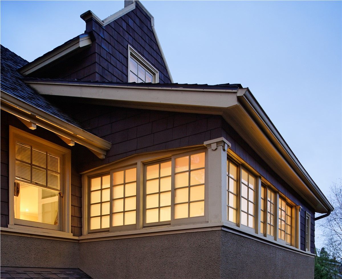 Exterior corner of a house at dusk, with illuminated windows. Brown siding and trim