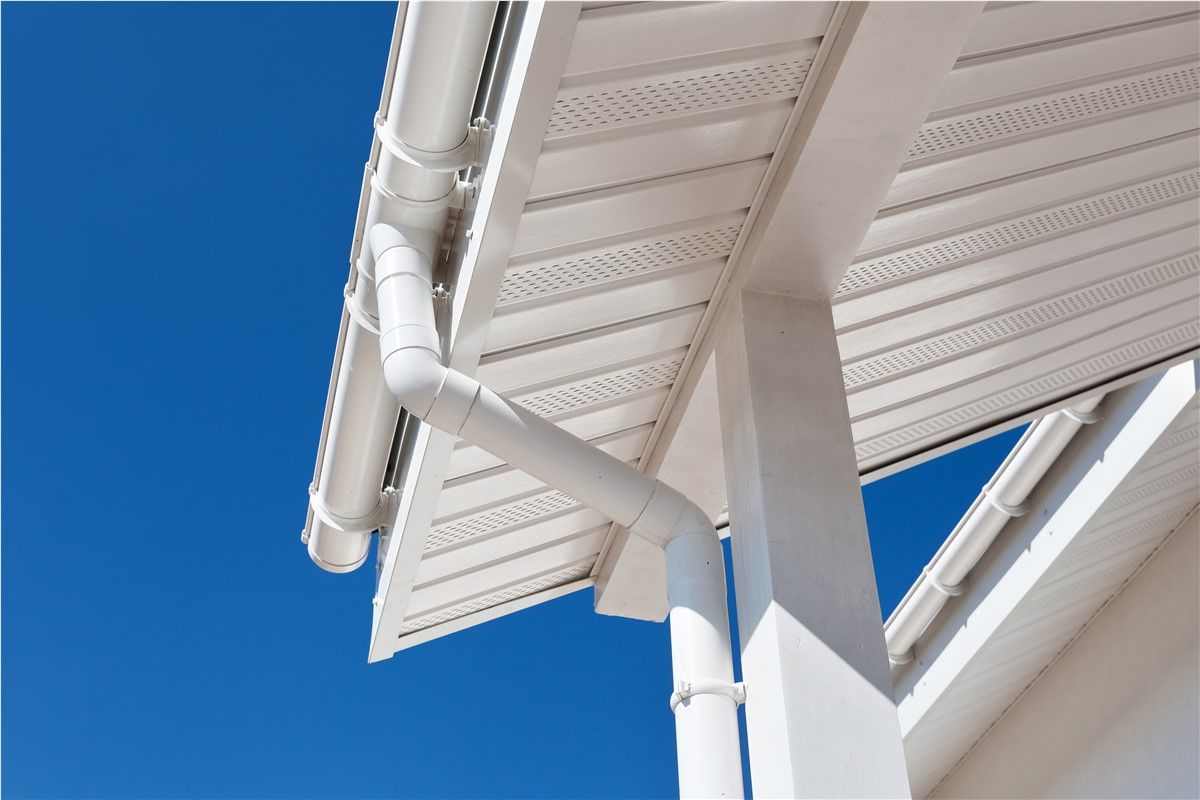 White gutters and downspout on a building's corner against a bright blue sky.