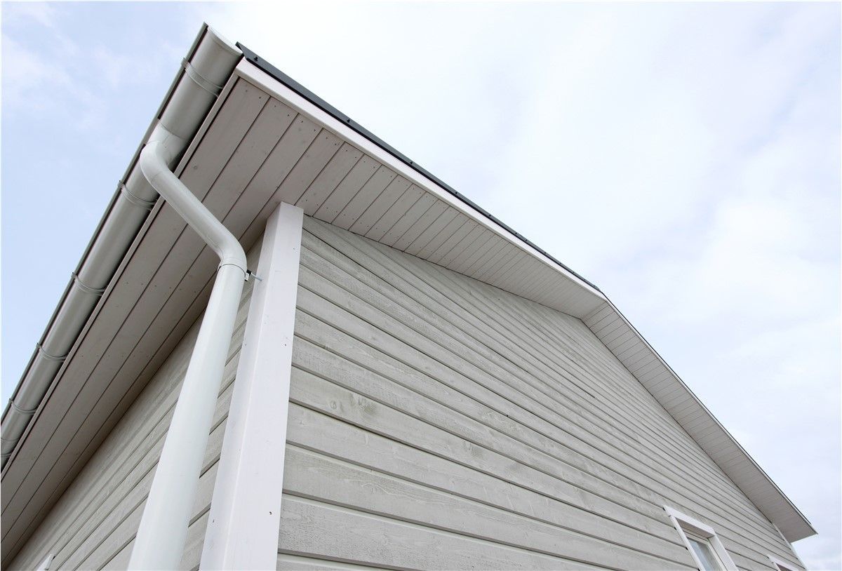 View from below of a light gray house with white trim, gutters, and siding against a cloudy sky.