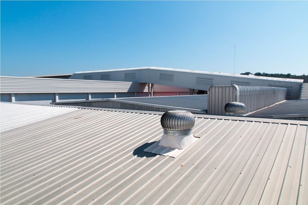 A metal roof with a spinning vent, under a clear blue sky. Buildings are in the background.