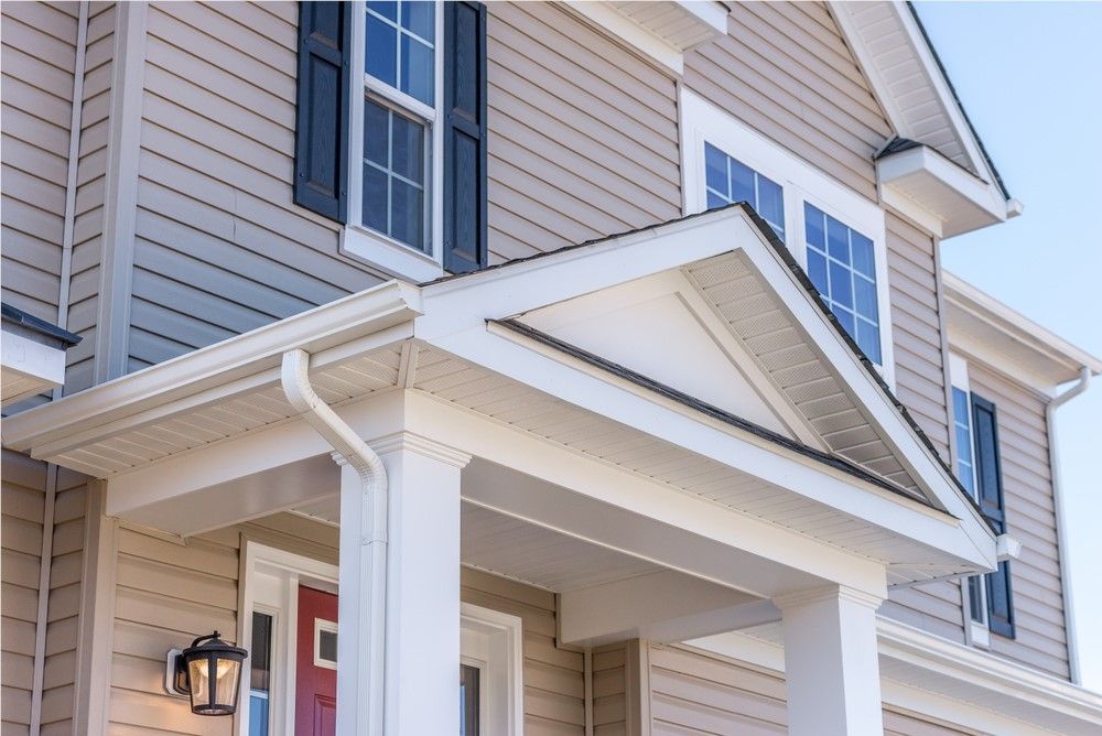 Tan house exterior with white trim, pillars, and red front door. Blue sky background.