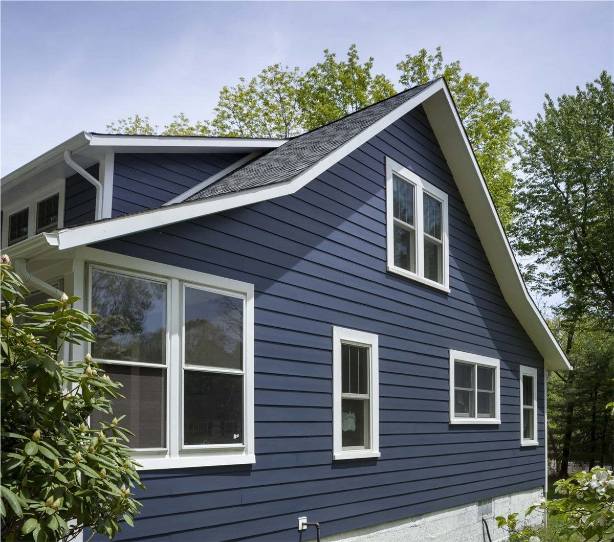 Navy blue house with white trim and multiple white-framed windows against a backdrop of trees and a bright blue sky.