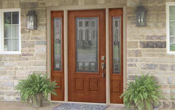 The front door of a brick house with a wooden door and two potted plants in front of it.