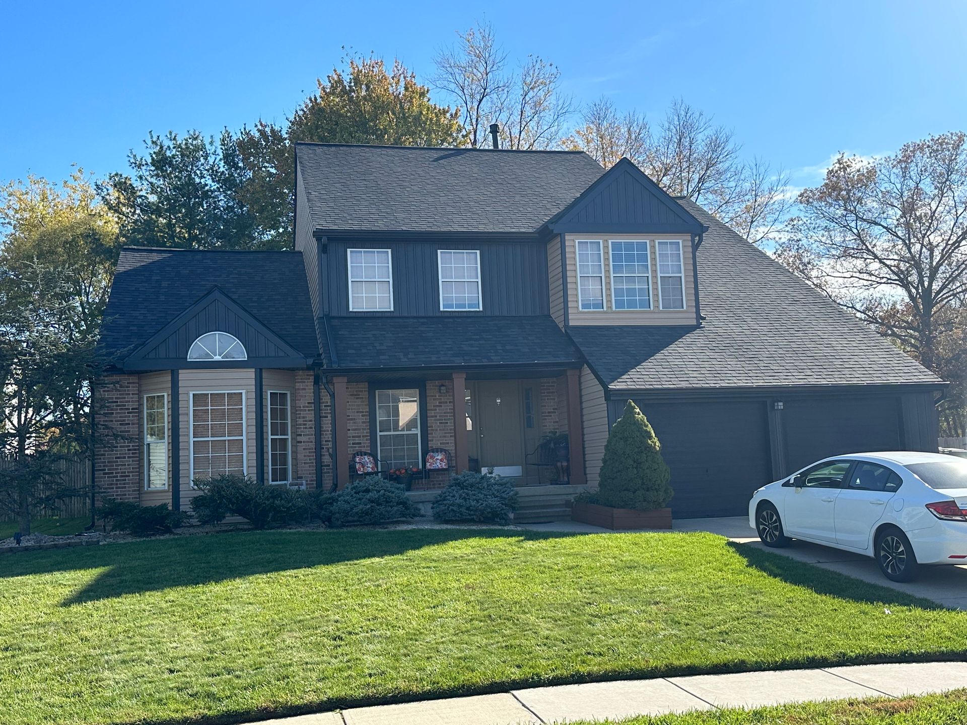 A two-story brick home with a dark roof and trim, a white car parked in the driveway, and green grass.